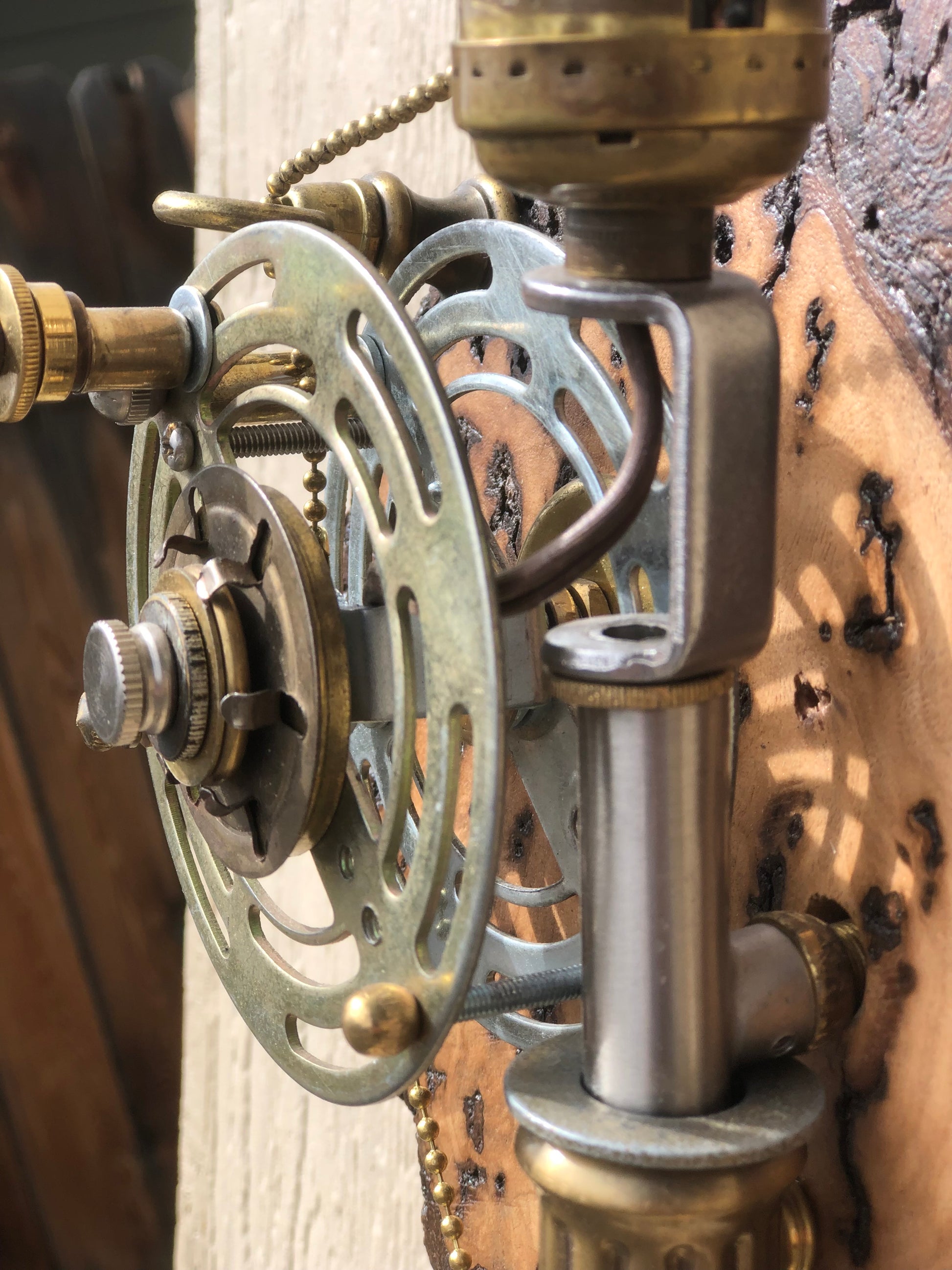 Close-up detail of the functional reel mechanism on Catch and Release. The brass and silver lamp-hardware reel is the operating switch — turning it pulls the beaded line through the rod and operates the lamp. Built from antique lamp parts by Random Brass.