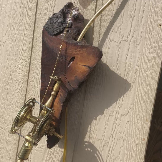 Video of Marlin, a wall-mounted sculptural fishing rod lamp by Random Brass. Demonstrates the reel mechanism in action — turning the brass reel pulls the beaded line, operating the lamp and lighting the Edison filament bulb mounted at the top of the curved gooseneck arm. Built from antique lamp parts on a charred reclaimed wood slab.